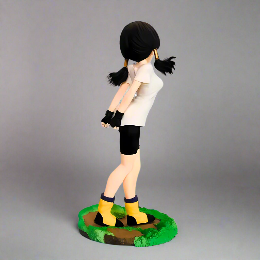 Figurine of a character with black hair styled in pigtails, wearing a white shirt, black shorts, and yellow shoes on a gray background.