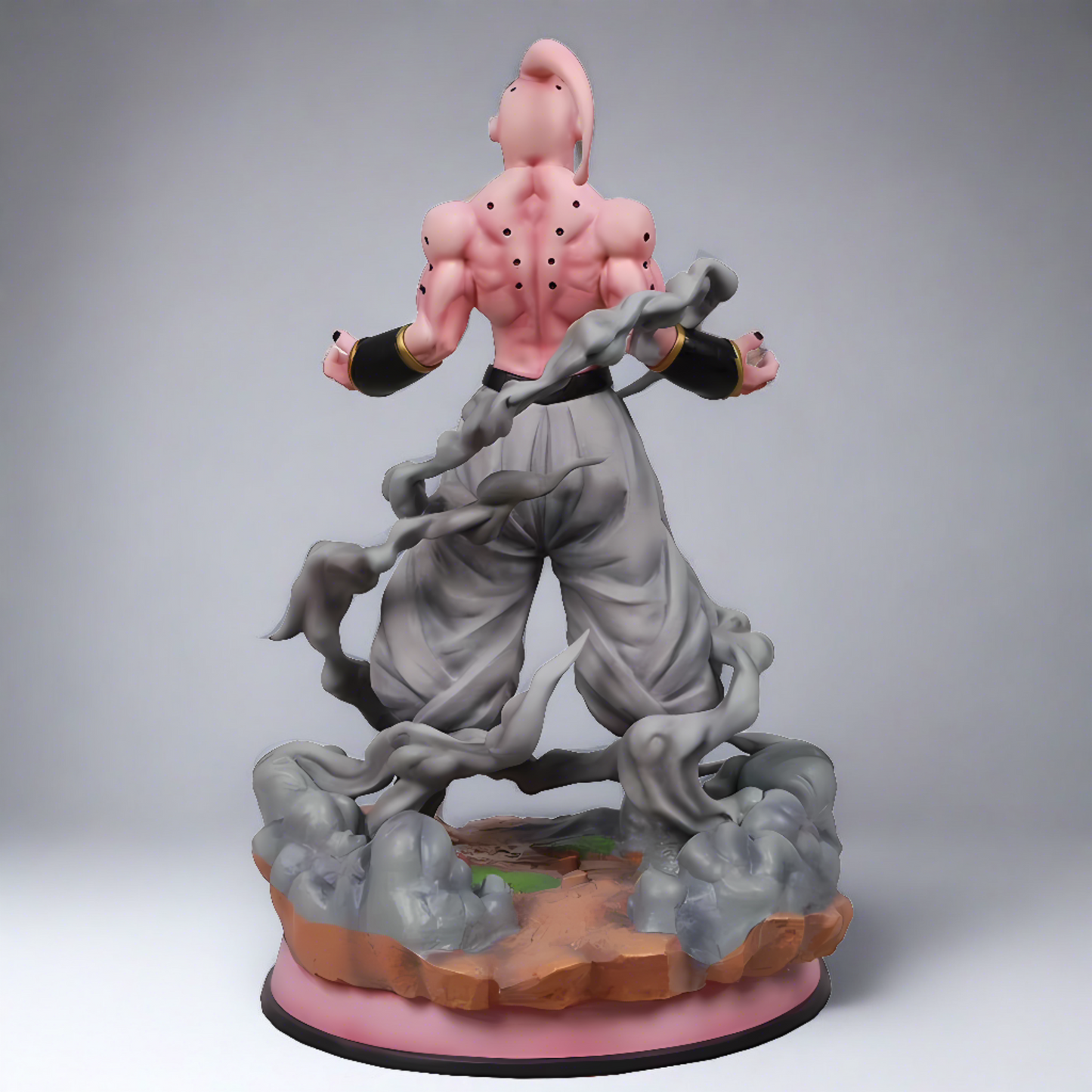 Rear view of Dragon Ball's Majin Buu collectible figure stands with a serene expression and arms outstretched, wearing grey pants and black wristbands, on a rocky base.