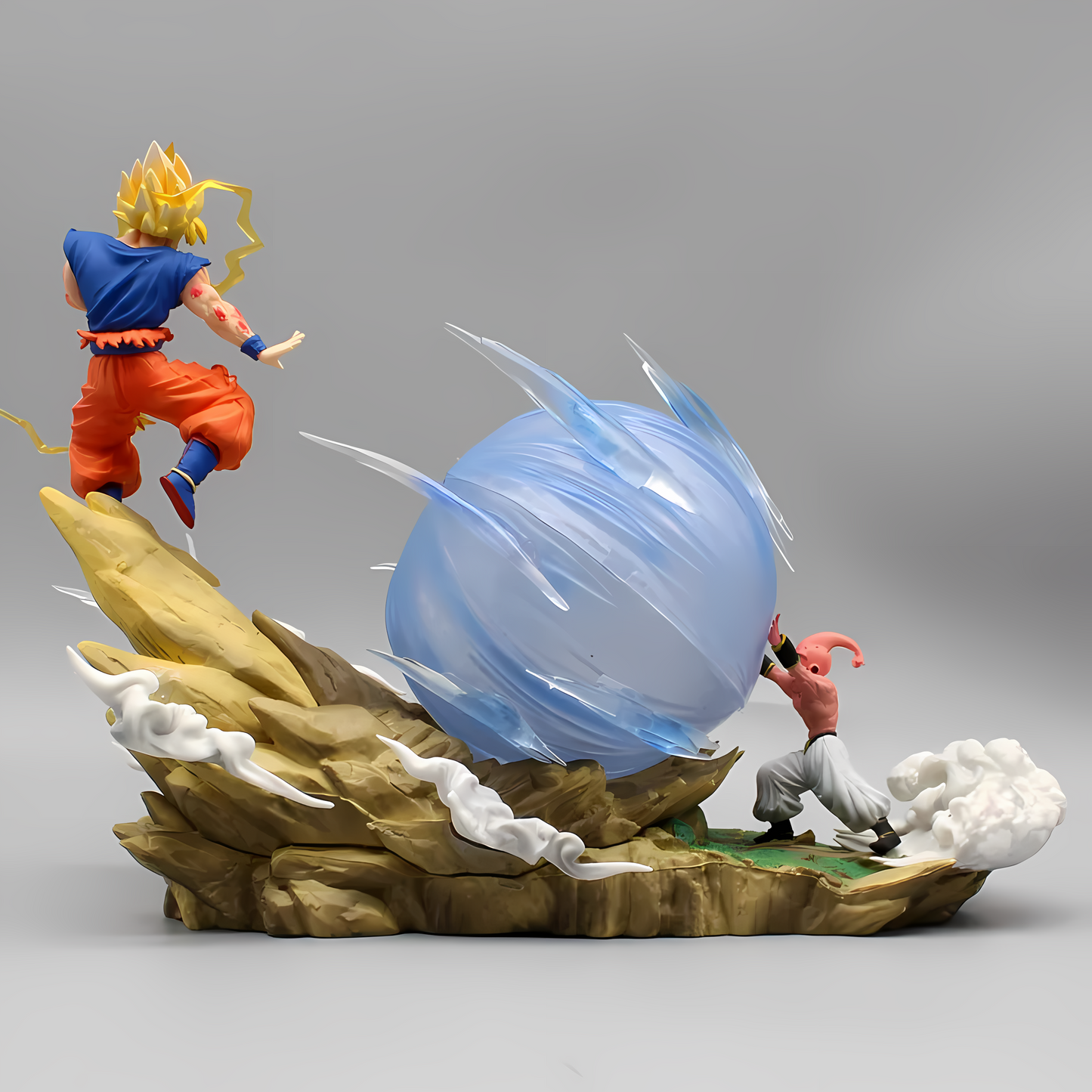 Collectible figure scene with Super Saiyan Goku mid-leap over a swirling blue energy ball launched by a concentrated Majin Buu on a rugged terrain base.
