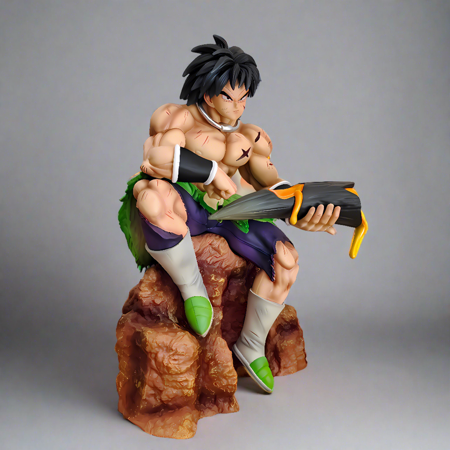 Collectible figure of Broly from Dragon Ball seated on a rock, reading a book amidst a fiery backdrop, showcasing his muscular physique and focused expression.