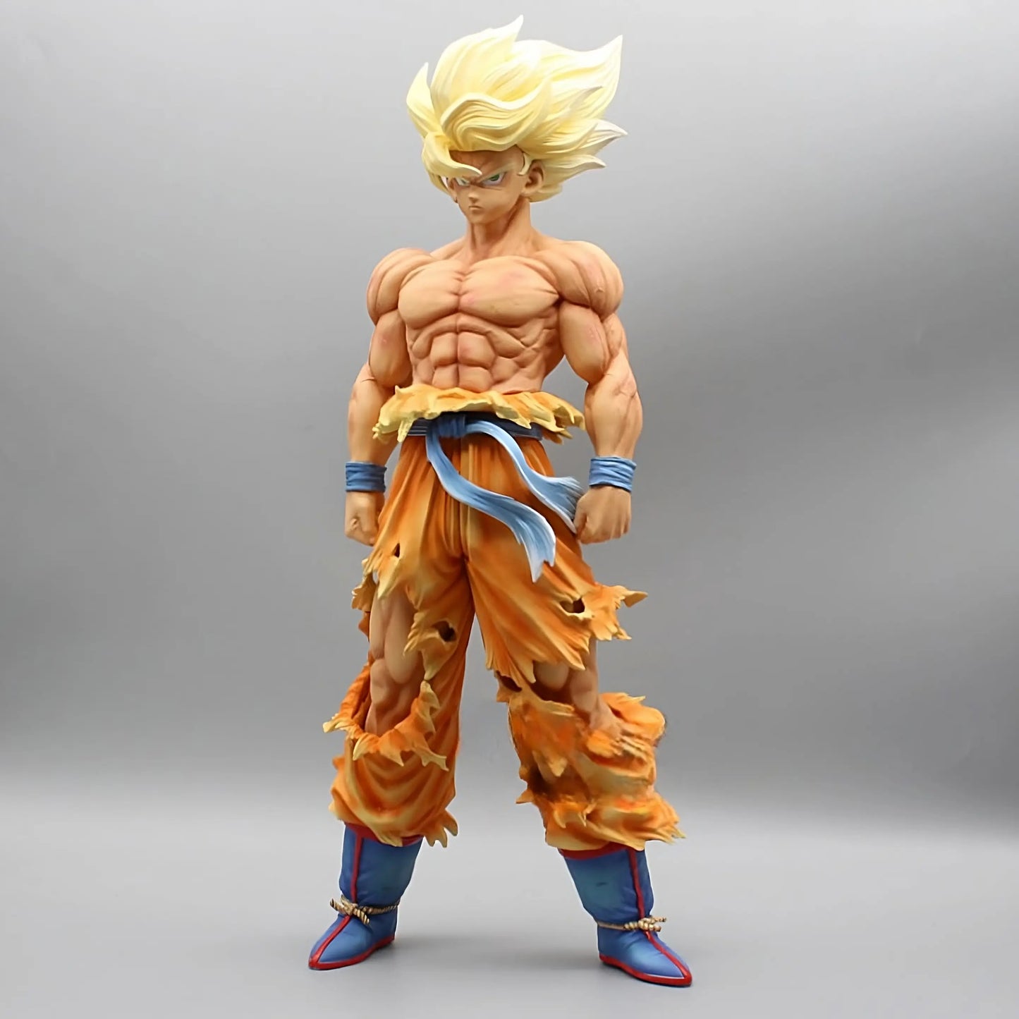 The 'Ascend to Saiyan Glory Goku' Dragon Ball collectible features a formidable Goku in Super Saiyan form, with his hair in the iconic golden spikes. He is captured in a strong stance, wearing a tattered orange gi over blue pants and red boots, highlighting his rippling muscles and the intense energy of his transformation, all against a simple gray backdrop.
