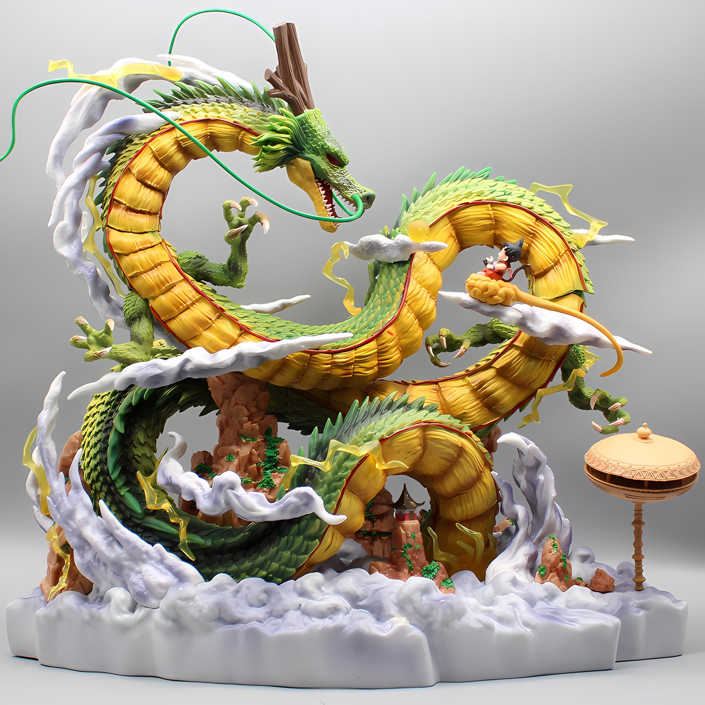 A meticulously crafted Dragon Ball Z collectible statue featuring the iconic Shenron, with a richly detailed design that highlights its serpentine body coiling around rocky formations and cloud-like accents. Goku, in miniature scale, is seen riding Shenron, while a single traditional pavilion stands elegantly to the side, all set against a plain gray backdrop.