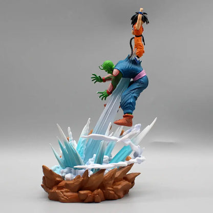 Figurine of Goku from Dragon Ball in mid-flight above Piccolo, both rising from an explosive energy base, depicted with vibrant colors and dynamic motion against a soft gray backdrop.
