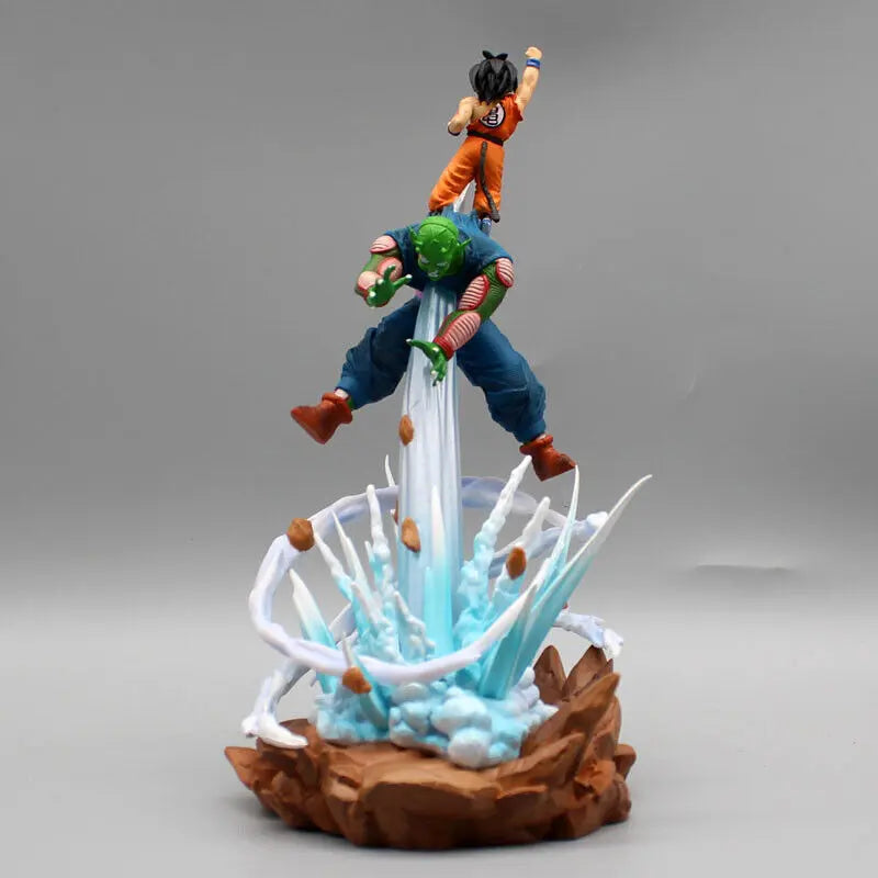 An action figure of Goku from Dragon Ball, positioned above Piccolo, with both characters suspended in motion amidst a dynamic splash of energy, on a simple gray backdrop.